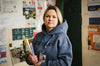 Woman in blue hoodie with documents and lanyard stands in front of info boards indoors